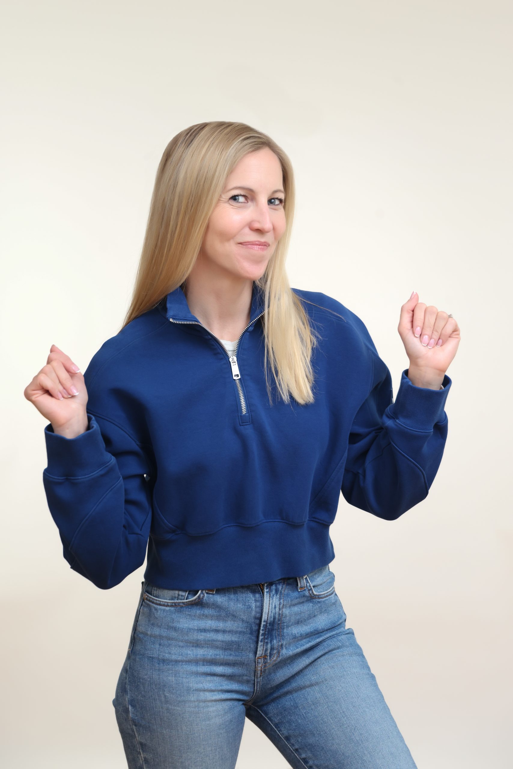 Kerri in a navy hoodie and jeans, smiling at the camera with her hands raised.