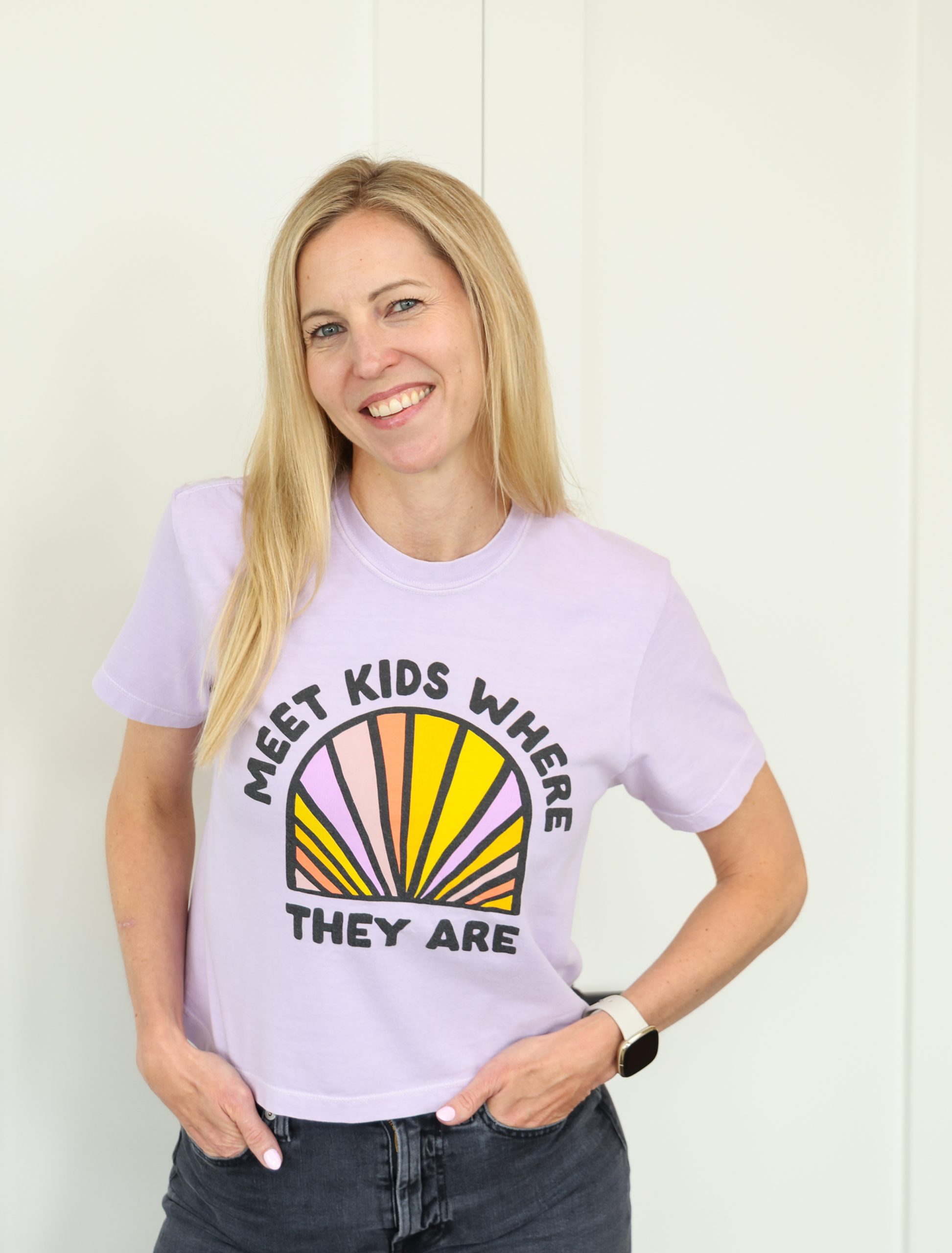 Kerri wearing a purple t-shirt that says "Meet kids where they are" and looking to her left with a smile on her face