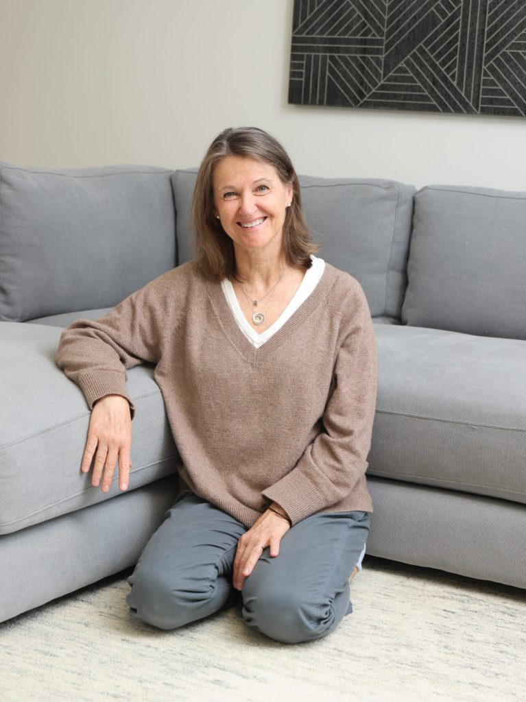 Therapy Keeper Team Member Holly sitting on the floor next to a sofa smiling at the camera